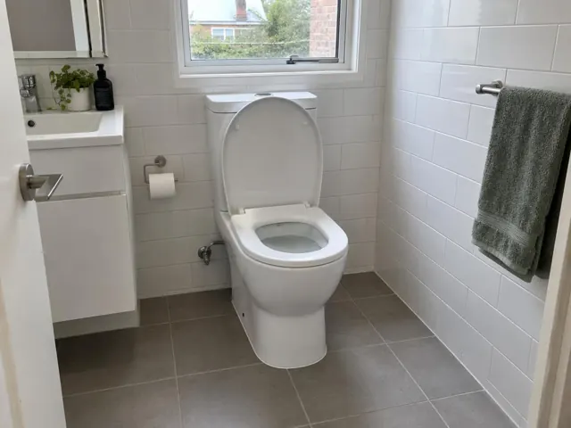 Clean white toilet in a tiled bathroom with vanity, window and towel rail in Newington