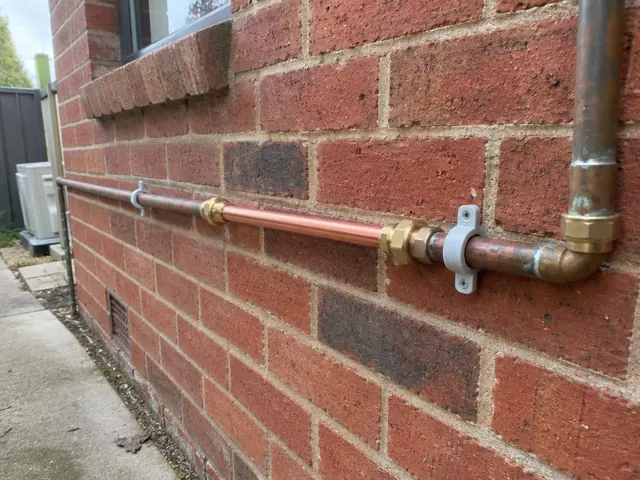 Repaired copper water pipe running along a brick exterior wall in Lidcombe